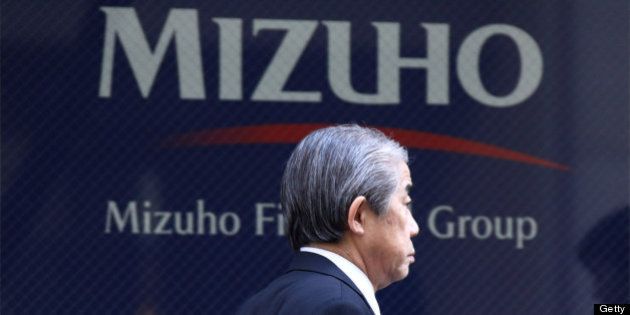 A pedestrian walks past the Mizuho Financial Group Inc. headquarters in Tokyo, Japan, on Tuesday, Feb. 26, 2013. Mizuho Financial Group Inc., Japan's third-biggest bank by market value, plans to cut an additional 600 jobs as it targets profit of 550 billion yen ($6 billion) in three years following the merger of its lending units. Photographer: Tomohiro Ohsumi/Bloomberg via Getty Images