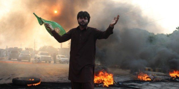 LAHORE, PAKISTAN - AUGUST 31: A supporter of the Pakistan Tehreek-e-Insaf (PTI) political party waves flag as they block the road with burning tires in Lahore, Pakistan on August 31, 2014. At least 4 people killed and more than 500 wounded in clashes between thousands of police and protesters in Pakistan's capital Islamabad Saturday, as a fortnight-long political impasse took a violent turn when opposition groups attempted to storm the prime minister's residence. (Photo by Rana Irfan Ali/Anadolu Agency/Getty Images)