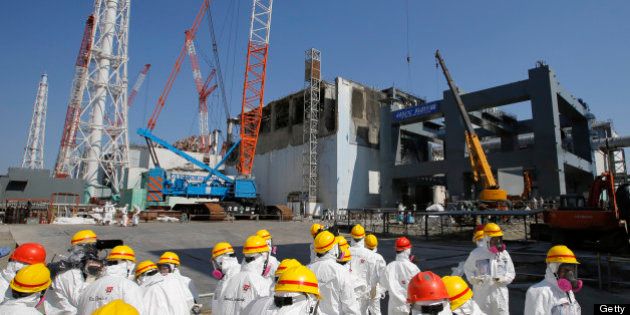 Members of the media and Tokyo Electric Power Co. (Tepco) employees, wearing protective suits and masks, visit the No. 4 reactor building, center, and the construction of a storage unit for melted fuel rods, right, at the company's Fukushima Dai-Ichi nuclear power plant in Okuma, Fukushima Prefecture, Japan, on Wednesday, March 6, 2013. Tepco's Fukushima Dai-Ichi plant had three reactor core meltdowns after it was hit by an earthquake and tsunami on March 11, 2011. Photographer: Issei Kato/Pool via Bloomberg