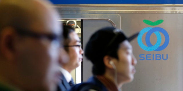 Passengers walk past the Seibu Railway Co. logo displayed on a train at a train station in Tokyo, Japan, on Monday, April 7, 2014. Seibu Holdings Inc. is targeting a price of 2,300 yen a share for an initial public offering by investors including Cerberus Capital Management LP, according to two people familiar with the matter. Photographer: Kiyoshi Ota/Bloomberg via Getty Images