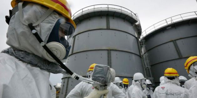 A Tokyo Electric Power Co. (Tepco) employee, left, wearing a protective suit and mask measures radiation as members of the media also in protective suits and masks stand in front of storage tanks for radioactive water at the Fukushima Dai-ichi nuclear power plant in Okuma, Fukushima Prefecture, Japan, on Thursday, Nov. 7, 2013. Tepco, which returned to profitability in its first-half earnings report on Oct. 31, is handling an estimated 11 trillion yen ($112 billion) cleanup of the nuclear plant wrecked by an earthquake and tsunami in 2011. Photographer: Kimimasa Mayama/Pool via Bloomberg