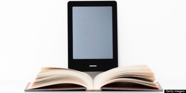 E-reader digital tablet resting on a shelf beside an open traditional paper book.