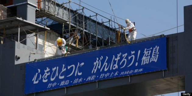 Workers wearing protective suits and masks stand on the construction site of a storage unit for melted fuel rods next to the No. 4 reactor building at Tokyo Electric Power Co.'s (Tepco) Fukushima Dai-Ichi nuclear power plant in Okuma, Fukushima Prefecture, Japan, on Wednesday, March 6, 2013. Tepco's Fukushima Dai-Ichi plant had three reactor core meltdowns after it was hit by an earthquake and tsunami on March 11, 2011. Photographer: Issei Kato/Pool via Bloomberg