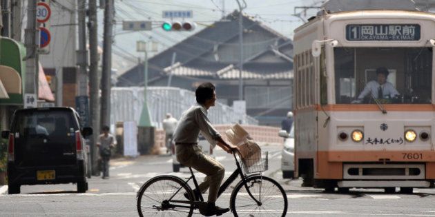 A man rides a bicycle past a tram in Okayama, Japan, on Tuesday, May 21, 2013. The Bank of Japan, forecast to maintain plans for expanded monetary easing at a meeting ending on May 22, is targeting 2 percent inflation in two years after more than 10 years of entrenched deflation. Photographer: Tomohiro Ohsumi/Bloomberg via Getty Images