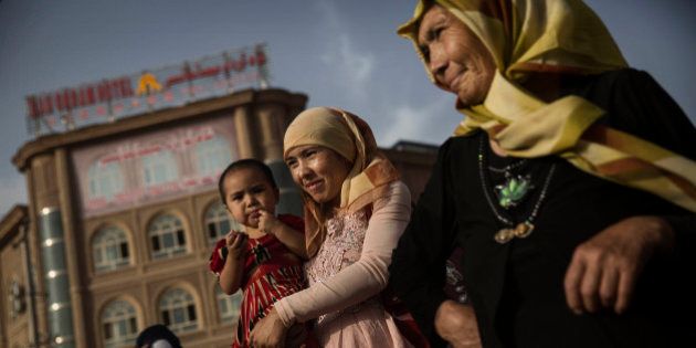 KASHGAR, CHINA - AUGUST 01: A Uyghur woman walks with her baby at a market on August 1, 2014 in old Kashgar, Xinjiang Province, China. Nearly 100 people have been killed in unrest in the restive Xinjiang Province in the last week in what authorities say is terrorism but advocacy groups claim is a result of a government crackdown to silence opposition to its policies. China's Muslim Uyghur ethnic group faces cultural and religious restrictions by the Chinese government. Beijing says it is investing heavily in the Xinjiang region but Uyghurs are increasingly dissatisfied with the influx of Han Chinese and uneven economic development. (Photo by Kevin Frayer/Getty Images)