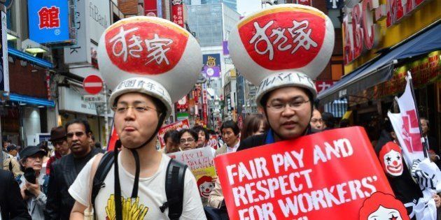 Labour union members wearing gear of Sukiya fast-food beef-bowl restaurant hold placards to demand payment of 1,500 yen (15 USD) an hour for part-time jobs during a march in Tokyo on May 15, 2014. Some 50 activists joined the global action to ask higher pay for part-time workers. AFP PHOTO / Yoshikazu TSUNO (Photo credit should read YOSHIKAZU TSUNO/AFP/Getty Images)