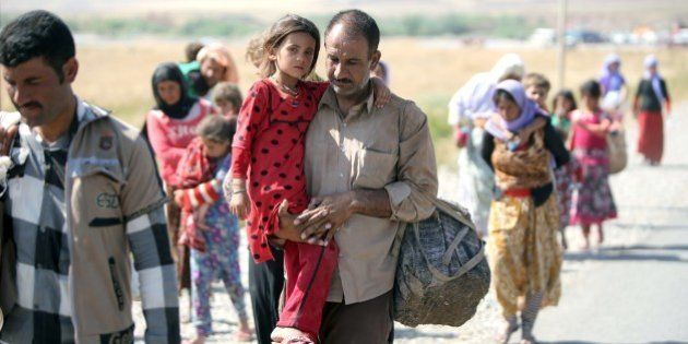 A displaced Iraqi man from the Yazidi community carries his daughter as they cross the Iraqi-Syrian border at the Fishkhabur crossing, in northern Iraq, on August 11, 2014. At least 20,000 civilians, most of whom are from the Yazidi community, who had been besieged by jihadists on a mountain in northern Iraq have safely escaped to Syria and been escorted by Kurdish forces back into Iraq, officials said. The breakthrough coincided with US air raids on Islamic State fighters in the Sinjar area of northwestern Iraq on August 9, and Kurdish forces from Iraq, Syria and Turkey working together to break the siege of Mount Sinjar and rescue the displaced. AFP PHOTO/AHMAD AL-RUBAYE (Photo credit should read AHMAD AL-RUBAYE/AFP/Getty Images)