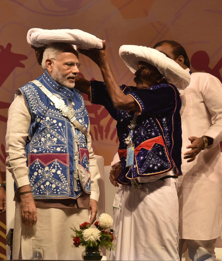 Prime Minister Narendra Modi, in tribal attire, being offered a traditional turban at the inauguration of the National Tribal Carnival-2016 on October 25, 2016 in New Delhi. Critics accuse Modi of focusing on optics at the cost of actual work. 