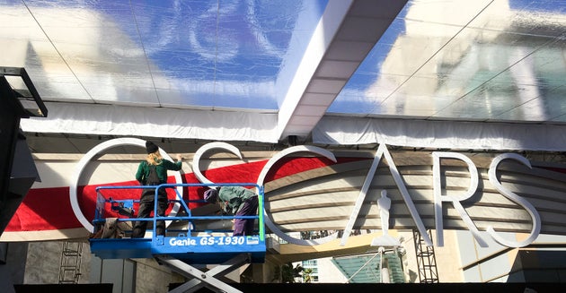 Τα συνεργεία βάφουν τα γράμματα που έχουν τοποθετηθεί πάνω από το κόκκινο χαλί.