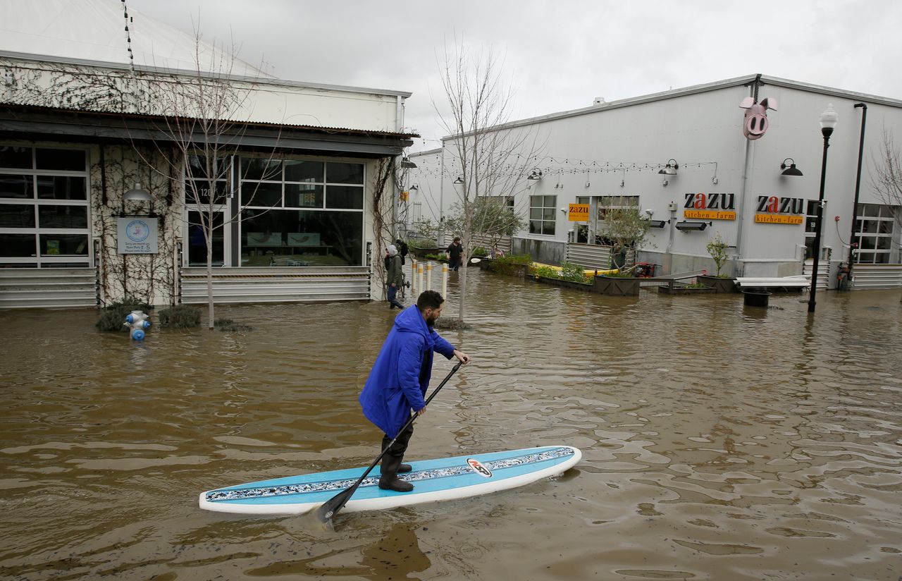 A man uses a paddleboard to make his way through the flooded Barlow Market District on Feb. 27, 2019, in Sebastopol, California.