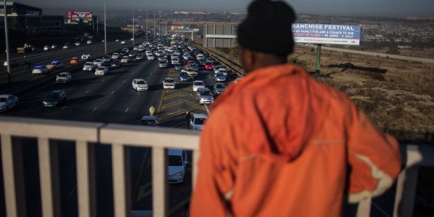 TOPSHOT - A bystander looks on from a bridge as traffic stands still as South African National Taxi Association members take part in a go slow action in Midrand on June 15, 2017, part of a nationwide protest against higher rates for financing their vehicles.The Department of Transport says the taxi strike in Midrand has been called off following an agreement between the South African National Taxi Association (Santaco) and SA Taxi Finance Holdings. / AFP PHOTO / MUJAHID SAFODIEN (Photo credit should read MUJAHID SAFODIEN/AFP/Getty Images)