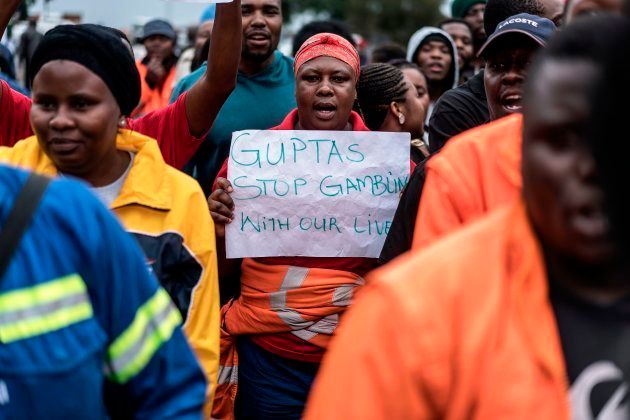 Employees and contractors of the Optimum coal mine in Hendrina, owned by the controversial Gupta family, demonstrate with a placard reading 'Guptas - stop gambling with our lives' in front of the gates of the mine on February 22, 2018. Workers are on strike because of the Bank of Baroda withdrawing services in South Africa and reduced the operations to a standstill as they marched to hand over a memorandum to the company's COO. / AFP