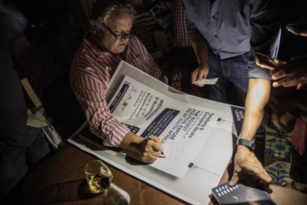 South African veteran investigative Journalist Jacques Pauw autographs books and a poster as a power failure occurs during the official presentation of his latest book 'The President's Keepers' in Johannesburg, South Africa on November 8, 2017.