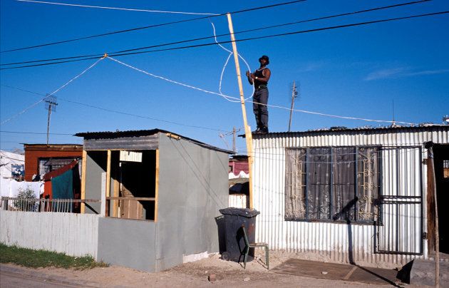 A man connects an electricity cable to his house on July 16, 2001 in Site B Khayelitsha, a township located approximately 21 miles outside Cape Town. Residents steal electricity from the municipality because they cannot afford to buy it.