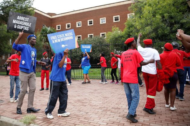 Protesters hold placards and chant slogans outside the Bloemfontein Regional Court where people, who were arrested after armed police raided the luxury home of the Gupta family, are to appear, in Bloemfontein, South Africa, February 15, 2018. REUTERS/Siphiwe Sibeko