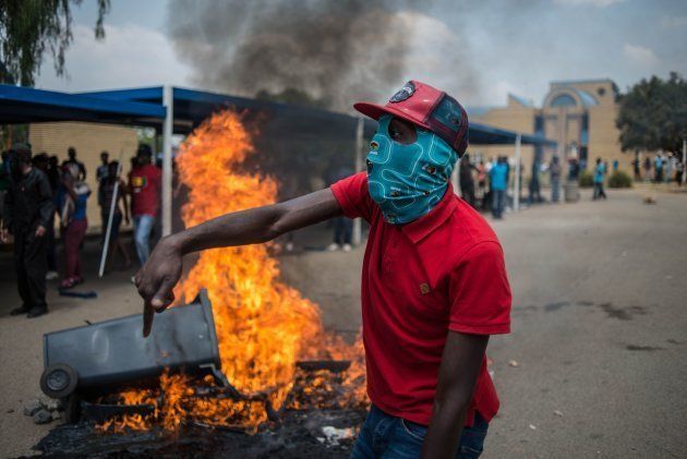 TOPSHOT - Students from Vaal University of Technology (VUT) shout slogans next to a burning barricade during clashes with South African anti-riot police and campus security at a demonstration in support of the Fees Must Fall Movement in Vanderbijlpark on October 13, 2016. Weeks of protests at South African universities have targeted tuition fees. / AFP / MUJAHID SAFODIEN (Photo credit should read MUJAHID SAFODIEN/AFP/Getty Images)