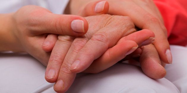 Caregiver holding elderly patients hand at home