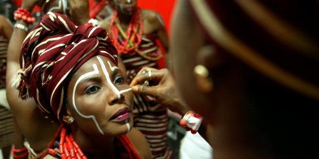 A woman has her face painted as she prepares to perform in traditional costume at the opening of the All Africa games in Nigeria's capital Abuja, October 4, 2003. Clothing in Nigeria symbolizes religious affiliation, wealth, and social standing and women wear wrap-around garments or dresses, typically made from very colorful materials, and beautiful head-ties that may be fashioned into elaborate patterns. RS/MA