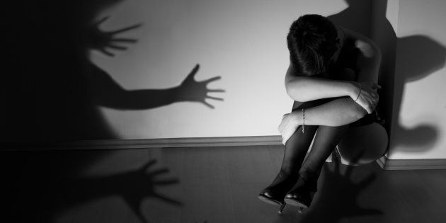 Photo of a woman with short black hair who is sitting huddled on the wooden floor sad and crying while the shadows in the shape of a hands are trying to grab her. Theme of the photo is fight against the violence against women.