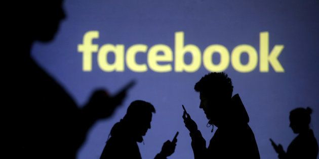 Silhouettes of mobile users are seen next to a screen projection of Facebook logo in this picture illustration taken March 28, 2018. REUTERS/Dado Ruvic/Illustration