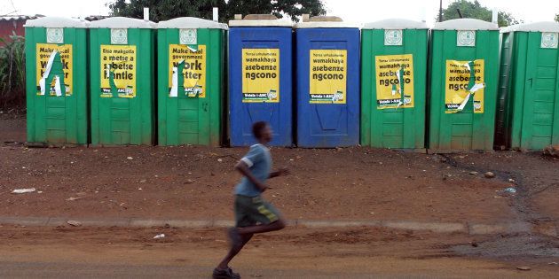 A young boy runs past communal toilets adorned with election posters for the ANC in Soweto township, outside Johannesburg, February 10, 2006.