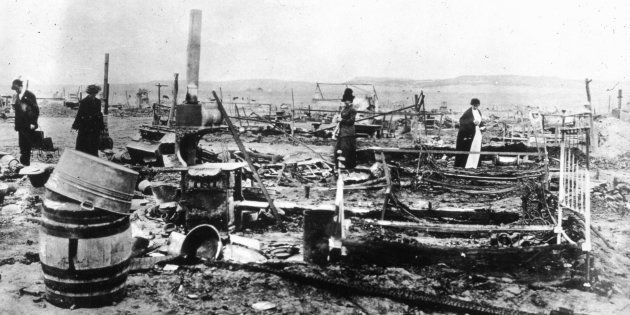 A group of people examining the ruins of the Ludlow colony in Colorado. Built as a temporary shelter for striking coal miners and their families, it was attacked by militiamen and company detectives who shot and burned to death eighteen people including eleven children, the youngest of whom was only three months old.