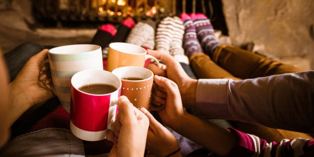 Four people warming their feet by the fireplace and drinking hot chocolate.