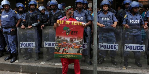 Riot police guard the entrance to a courthouse in Pretoria, South Africa, Wednesday, Nov. 2, 2016, as an Economic Freedom Fighters supporter protests. Thousands of South Africans are demonstrating for the resignation of President Jacob Zuma, who has been enmeshed in scandals that critics say are undermining the country's democracy.