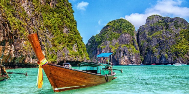 Long tail wooden boat at Maya Bay on Ko Phi Phi Le, made famous by the movie titled 'The Beach'. Beautiful cloudscape over the turquoise water and green rocks in Maya Bay, Phi Phi Islands, Thailand.