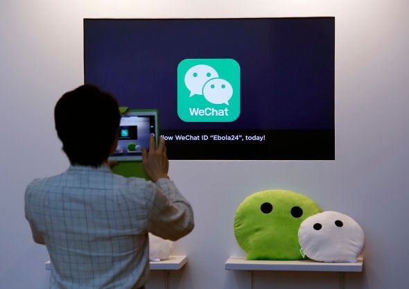A man takes a photograph of a counter promoting WeChat, a product of Tencent, displayed at a news conference announcing the company's results in Hong Kong March 18, 2015.