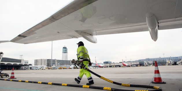 A ground crew worker carries a fuel pipe under a passenger aircraft.