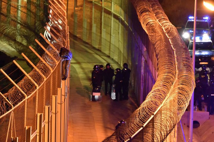 An African migrant stands on top of a border fence as Spanish police stand guard below during a failed attempt to cross into Spanish territories, between Morocco and Spain's north African enclave of Ceuta, January 1, 2017. REUTERS/Jose Antonio Sempere