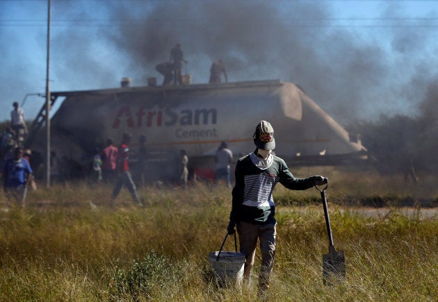 A local carries a bucket and a spade, after looting cement from an AfriSam cement truck during protests in Mahikeng, North West Province, South Africa, April 20, 2018.