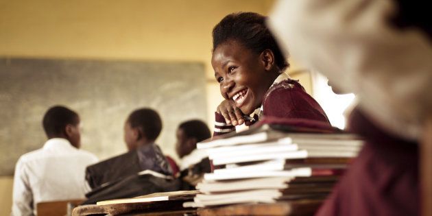 A Happy young South African girl (from the Xhosa tribe) works on her studies and jokes with her friends at at an old worn desk in a class room in the Transkei region of rural South Africa.