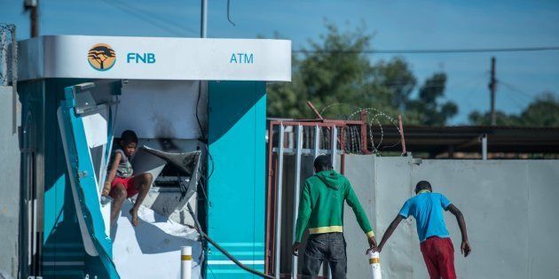 Children play around a vandalised ATM in North West on April 20, 2018, as protests continued for a second day in provincial capital Mahikeng. Police fired rubber bullets at protesters after President Cyril Ramaphosa cut short a foreign trip to deal with violent riots over alleged government corruption and poor public services. Shops were looted, roads were blocked and vehicles set alight. At least 23 people were arrested, and one man was reported to have died.