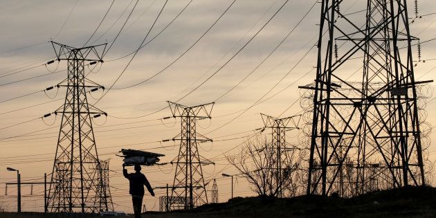 A woman carries fire wood on her head as she walks below state power utility ESKOM's elecricity pylons in Soweto, South Africa, August 8, 2016. Picture taken August 8, 2016. REUTERS/Siphiwe Sibeko/File Photo