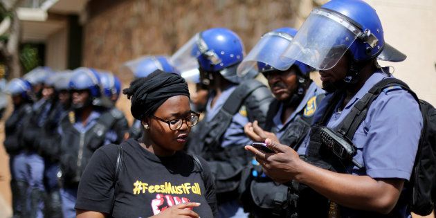 A student (wearing a 'FEES MUST FALL' t-shirt) chats to a riot police officer as they stand guard outside Hillbrow magistrate court during an appearance of students who were arrested during a protest demanding free education at the Johannesburg's University of the Witwatersrand, South Africa, October 12, 2016. REUTERS/Siphiwe Sibeko