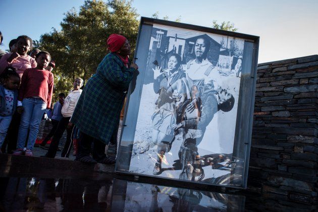 Ms Nontsikelelo Makhubu is seen next to the iconic photograph by Sam Nzima showing a dying Hector Pieterson carried away during the start of the Soweto Uprising in 1976, during celebrations to commemorate the 40th anniversary of the day, on June 16 2016 in Soweto. (JOHN WESSELS/AFP/Getty Images)