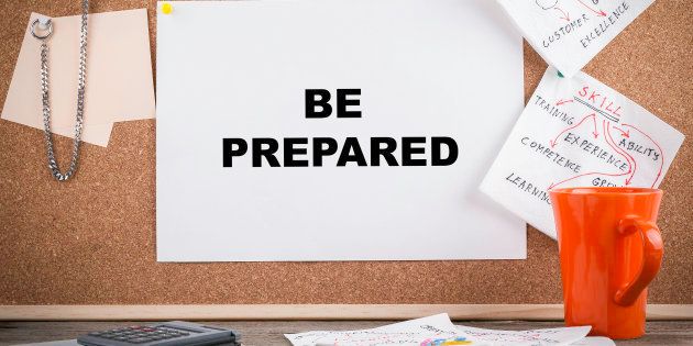 BE PREPARED. Text on cork board. Wooden office desk with a big mess