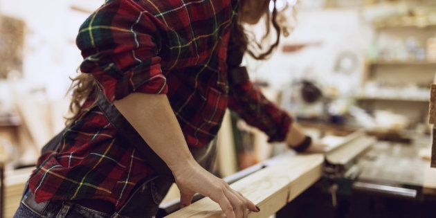 Woman Carpenter working on an electric buzz saw cutting some boards