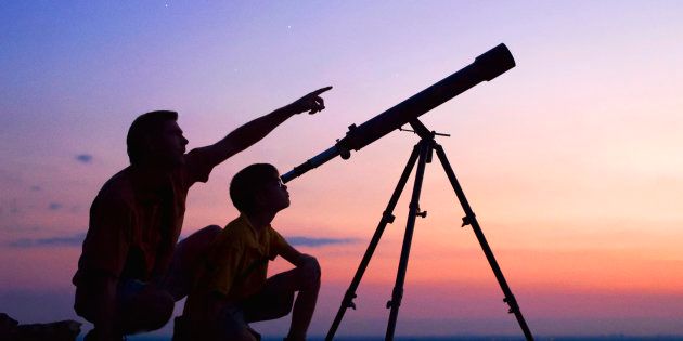A young boy looking thru a telescope at sunset with his father.