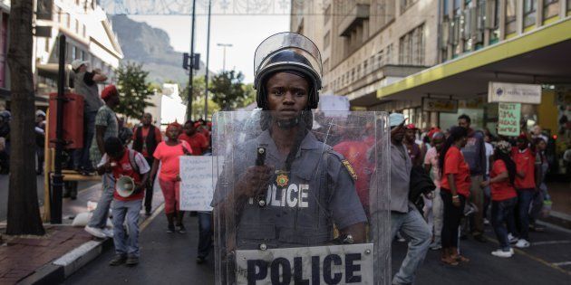 A South African riot policeman stands by as South African opposition party Economic Freedom Fighters (EFF) members and supporters sing and dance while shouting slogans against the South African president ahead of the annual State Of The Nation Address (SONA) on February 9, 2017 in Cape Town.