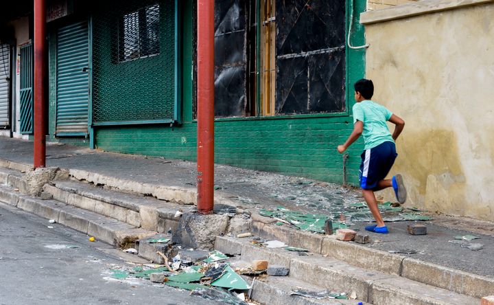 A boy runs past a damaged building in Rossettenville during clashes between residents on February 12, 2017 in Johannesburg. At least 12 houses were torched in the area during a weekend of violence after police raided the area last week. Residents claim the burned houses are used as drug dens and brothels.