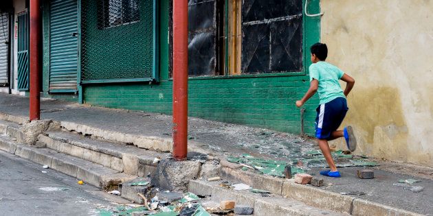 A boy runs past a damaged building in Rosettenville during clashes between residents on February 12, 2017 in Johannesburg. At least 12 houses were torched in the area during a weekend of violence after police raided the area last week. Residents claim the burned houses are used as drug dens and brothels.