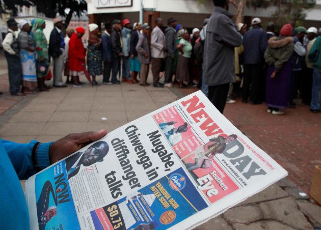 A man reads a newspaper as residents queue to draw money at a bank in Harare, Zimbabwe, November 17, 2017.