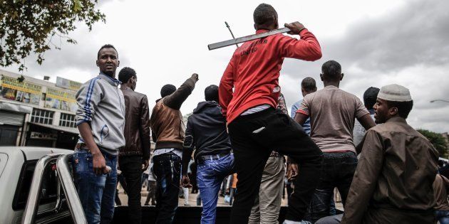 Somali migrants armed with rocks and sticks watch from the back of a pick up truck as a police helicopter hover over an anti-immigration march in the Marabastad neighbourhood in Pretoria on February 24, 2017.