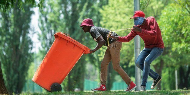 A student from Vaal University of Technology (VUT) hurls stones as he is flanked by another student taking cover behind a plastic bin during clashes with South African anti-riot police and campus security at a demonstration in support of the Fees Must Fall Movement in Vanderbijlpark on October 13, 2016.