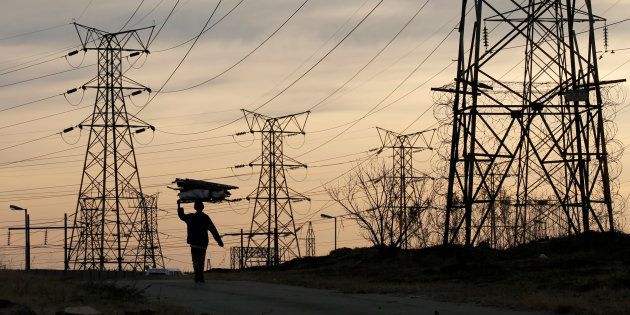 A woman carries fire wood on her head as she walks below state power utility ESKOM's elecricity pylons in Soweto, South Africa, August 8, 2016. Picture taken August 8, 2016. REUTERS/Siphiwe Sibeko/File Photo