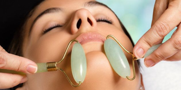 Macro close up portrait of woman having facial beauty treatment in spa. Therapist massaging chin with jade rollers.