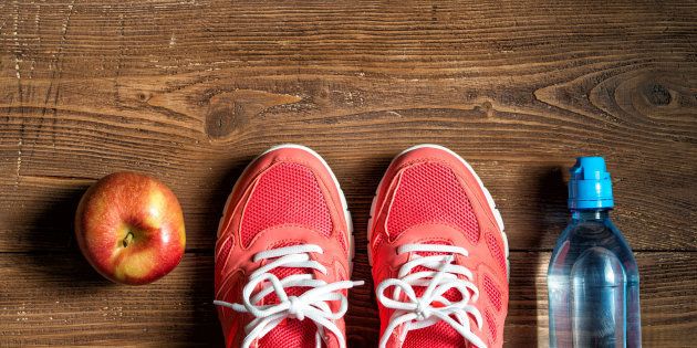 Fitness concept, pink sneakers, red apple and bottle of water on wooden background, top view